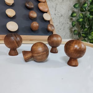 May include: Four wooden knobs with a rounded top and a small base. The knobs are a dark brown color and have a wood grain pattern.