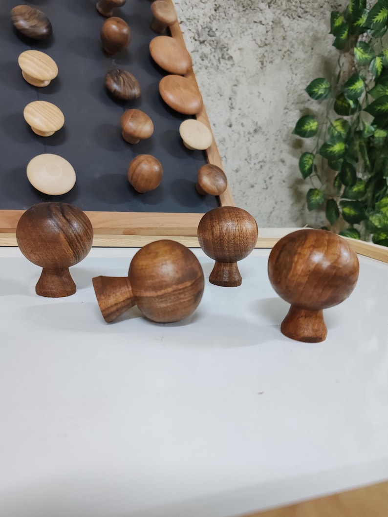 May include: Four wooden knobs with a rounded top and a small base. The knobs are a dark brown color and have a wood grain pattern.