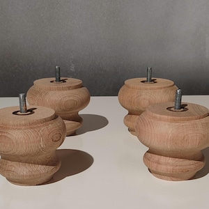 Könnte beinhalten: Vier unfertige Holzmöbelfüße mit gedrehtem Design. Jeder Fuß hat eine runde, bauchige Form und einen Gewindebolzen, der aus der Oberseite herausragt. Die Beine sind hellbraun und stehen auf einer weißen Oberfläche.
