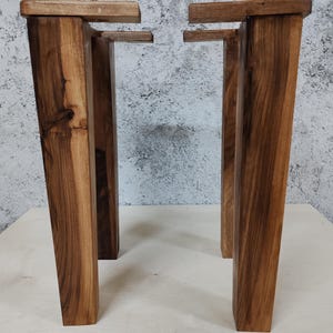 May include: Two sets of wooden table legs, each set consisting of two legs with a rectangular top and a square bottom. The legs are a dark brown colour and have a natural wood grain.