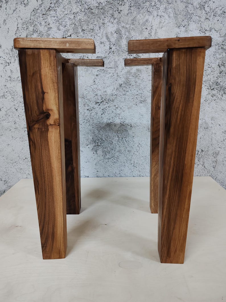 May include: Two sets of wooden table legs, each set consisting of two legs with a rectangular top and a square bottom. The legs are a dark brown colour and have a natural wood grain.