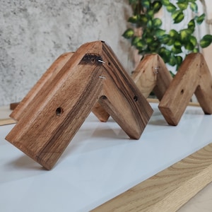 May include: Three wooden wall hooks in the shape of a chevron, arranged in a row. The hooks are made of dark brown wood with a natural grain pattern.