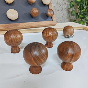 May include: Five wooden knobs with a dark brown finish. The knobs have a round shape with a slightly raised base. The knobs are arranged on a white surface.