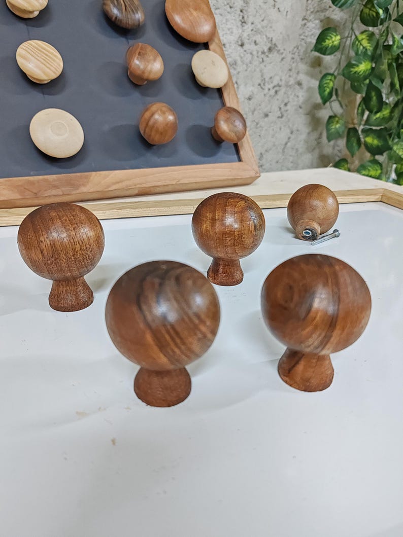 May include: Five wooden knobs with a dark brown finish. The knobs have a round shape with a slightly raised base. The knobs are arranged on a white surface.