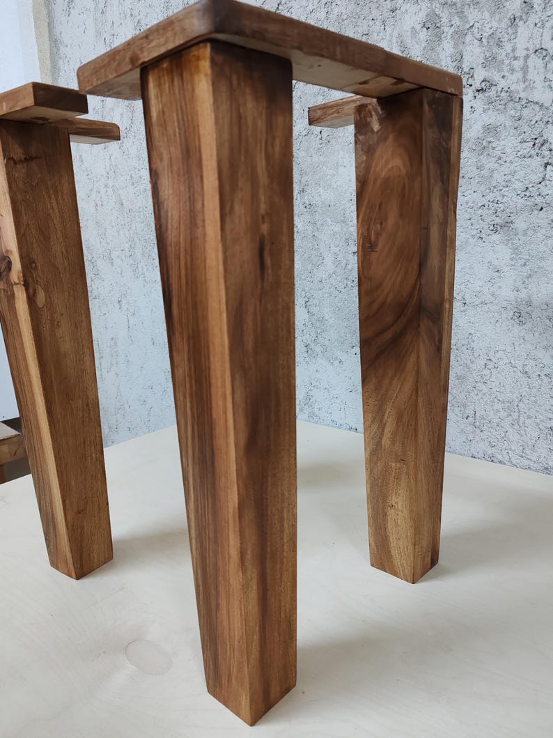 May include: Two wooden table legs with a dark brown stain. The legs are square and have a slightly tapered shape. The legs are made of solid wood and have a natural grain pattern.