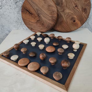 May include: A collection of wooden knobs in various shades of brown and cream arranged on a black surface with a wooden frame. The knobs are displayed in a grid pattern.