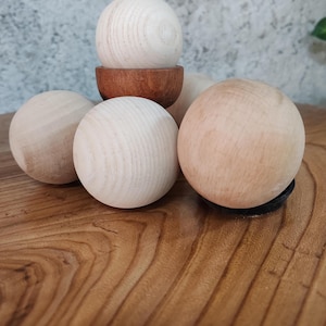 Op de afbeelding: Vijf houten ballen, waarvan vier lichtbruin zijn en één iets donkerder bruin. De ballen zijn in een piramidevorm op een houten oppervlak gerangschikt.