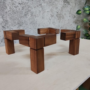 May include: A wooden table stand made of multiple connected blocks. The stand is made of dark brown wood and has a rectangular shape. The stand is sitting on a light brown surface.