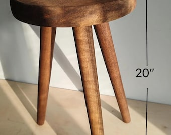 May include: A wooden stool with a round top and three legs. The stool is 10 inches wide and 20 inches tall.