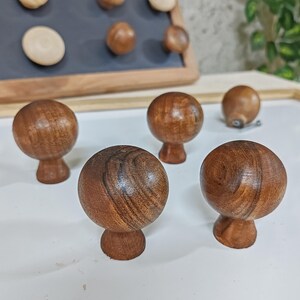 May include: Four wooden knobs with a mushroom shape and a dark brown wood grain finish. The knobs are arranged on a white surface.