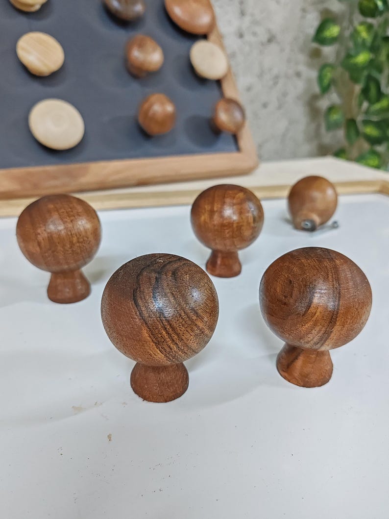 May include: Four wooden knobs with a mushroom shape and a dark brown wood grain finish. The knobs are arranged on a white surface.