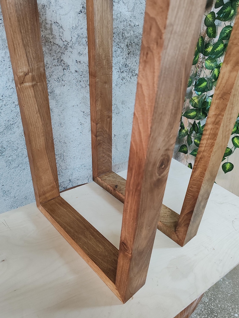 Puede incluir: Dos marcos de madera, cada uno con forma cuadrada, est&aacute;n unidos en la parte superior. Los marcos son de madera marr&oacute;n oscura con un patr&oacute;n de veta natural. Los marcos est&aacute;n sobre una superficie marr&oacute;n claro.