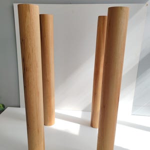 May include: Four unfinished wooden furniture legs. The legs are cylindrical, with a light brown color and a smooth finish. They are arranged in a group, suggesting they are ready for assembly into a table or other furniture piece.