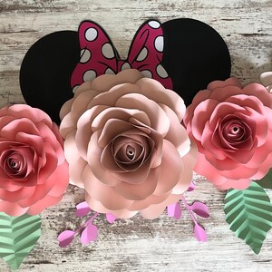 May include: A paper craft decoration featuring a pink and white floral arrangement with a black and red Minnie Mouse ears in the center. The flowers are made of paper and have a layered, three-dimensional effect.