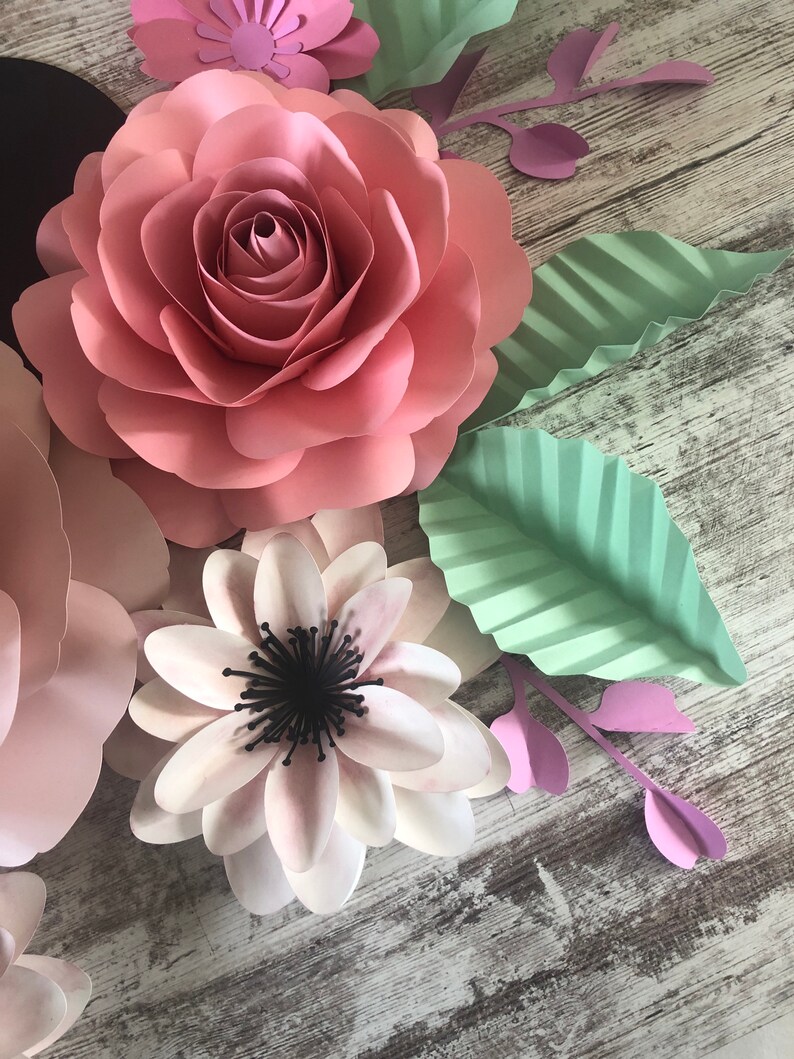 May include: A set of paper flowers in pink, white, and green. The flowers are layered and have a delicate, handmade look.