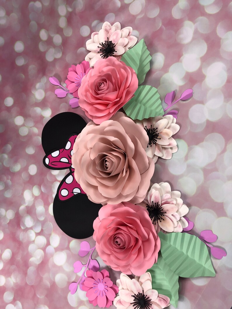 May include: A pink and white paper flower arrangement with a black and red Minnie Mouse bow. The flowers are layered and have a 3D effect.