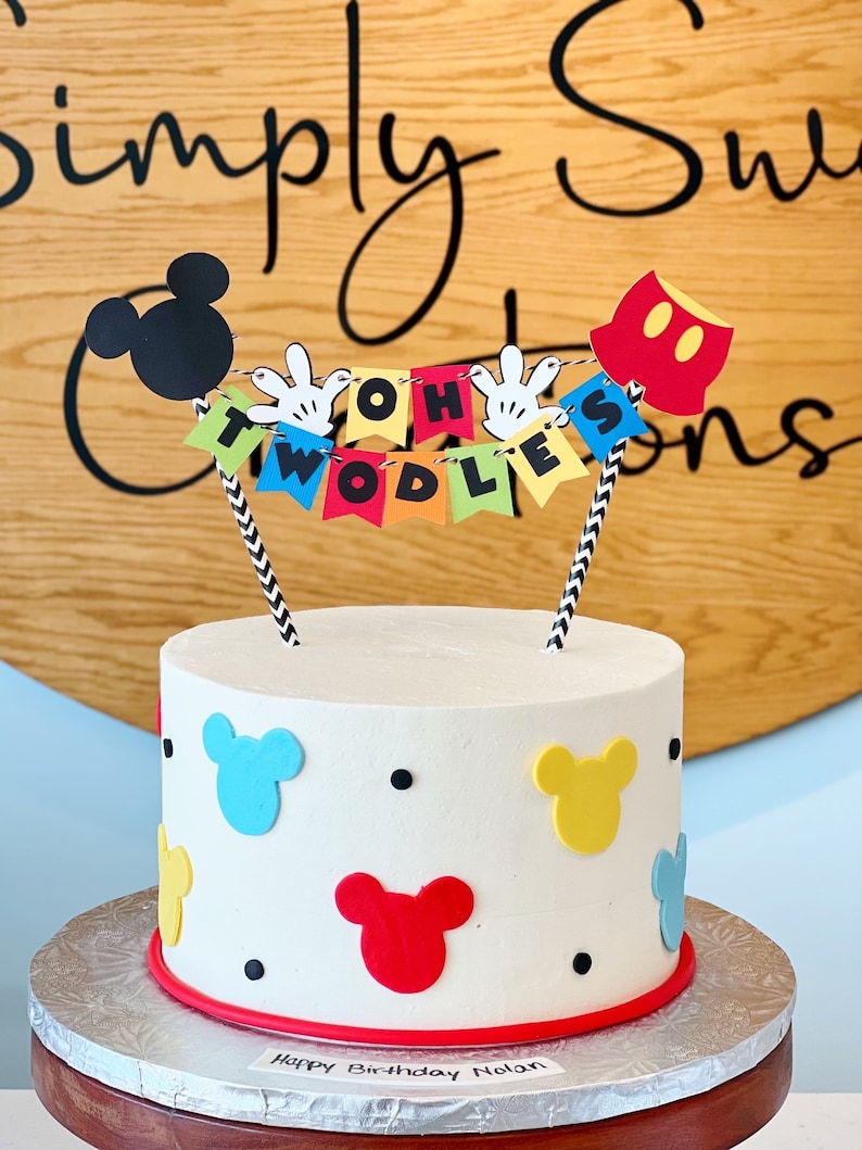 Peut inclure: Un g&acirc;teau blanc d&eacute;cor&eacute; avec des oreilles de Mickey Mouse et les mots "Oh Two-dles" sur une banni&egrave;re. Le g&acirc;teau est sur un support &agrave; g&acirc;teau argent&eacute; et a une bordure rouge. Le g&acirc;teau est d&eacute;cor&eacute; de points noirs et d'oreilles de Mickey Mouse en bleu, jaune et rouge.