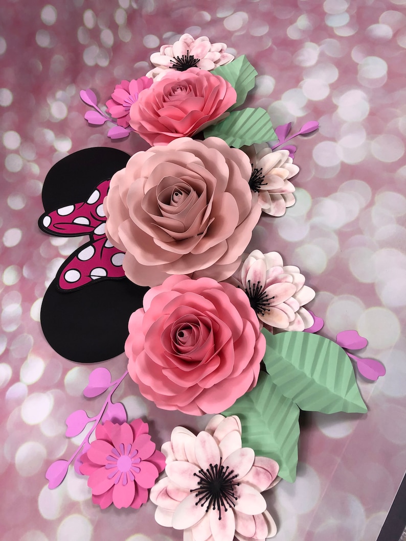 May include: A paper flower arrangement featuring pink and white roses, pink and purple flowers, and green leaves. The arrangement includes a black and red paper Mickey Mouse ears.
