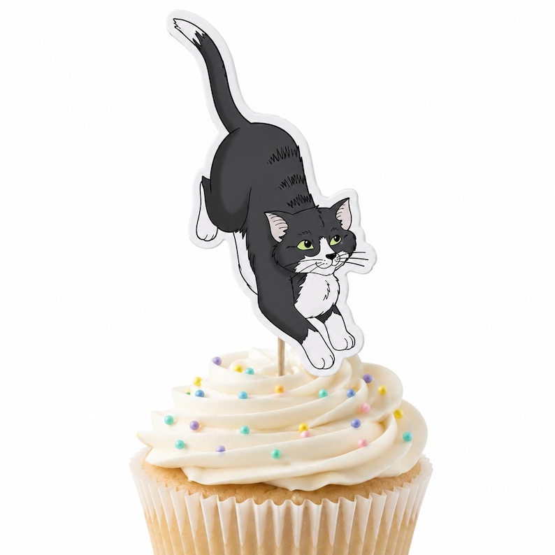 May include: A cupcake topper featuring a black and white cat illustration in a pouncing pose, attached to a wooden pick. The cupcake is topped with white frosting and decorated with small, multicolored round sprinkles scattered across the surface.