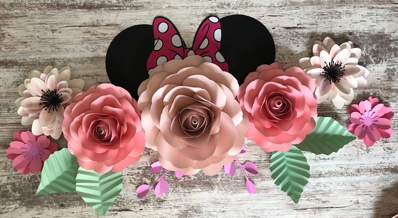 May include: A paper craft decoration featuring a pink and white floral arrangement with a black and red Minnie Mouse ears in the center. The flowers are made of paper and have a layered, three-dimensional effect.
