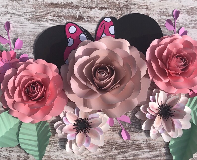 May include: A set of paper flowers in shades of pink and white, with a black and red Minnie Mouse ears cutout in the center. The flowers are arranged in a semi-circle, with the Minnie Mouse ears in the center.