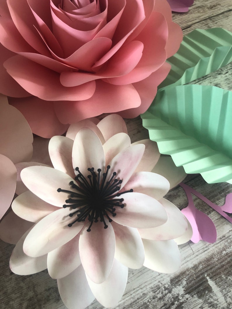May include: A close-up of a paper flower craft. The flower is white with a black center and pink edges. The flower is surrounded by other paper flowers in pink and green.