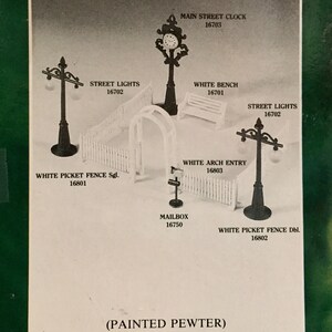 May include: A collection of painted pewter miniature accessories including a Main Street Clock 16703, Street Lights 16702, White Bench 16701, White Picket Fence Sgl 16801, White Arch Entry 16803, Mailbox 16750, and White Picket Fence Dbl 16802.