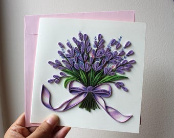 Könnte beinhalten: Handgefertigte Grußkarte mit einem Quilling-Lavendelstrauß mit lila und grünen Details. Der Strauß ist mit einem lila Band gebunden. Die Karte befindet sich auf einem weißen Hintergrund mit einem rosa Umschlag.