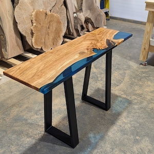 May include: A wooden table with a blue resin inlay and black metal legs. The table is made of natural wood with a unique grain pattern.