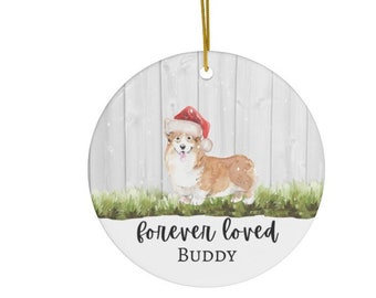 May include: A white ceramic Christmas ornament with a watercolor illustration of a corgi wearing a Santa hat. The ornament has the text "forever loved" and "BUDDY" on it.