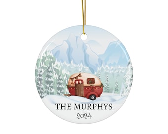 Op de afbeelding: Een witte keramische kerstbal met een rode en witte camper in een besneeuwd berglandschap. De tekst "THE MURPHYS 2024" staat op de kerstbal.