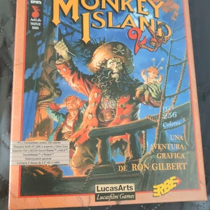 Puede incluir: Caja de juego de PC vintage de "Monkey Island 2: LeChuck's Revenge". La ilustración muestra un pirata con rostro de calavera, un barco y el título del juego en letras naranjas. La caja también incluye texto sobre los requisitos y características del juego.