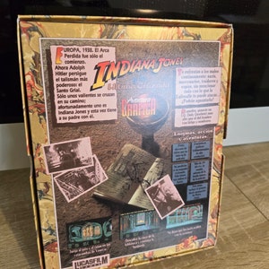 May include: A vintage Indiana Jones video game box. The box features the title "Indiana Jones: The Last Crusade" with graphics and text in Spanish. The box has a gold and brown colour scheme with images from the movie.