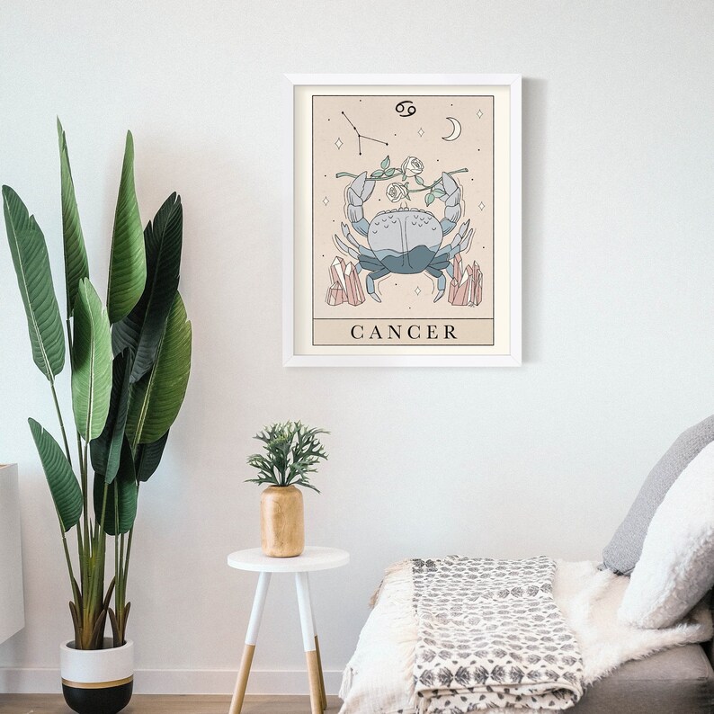 May include: A white framed print with a beige background featuring a blue crab with pink crystals and a white rose. The crab is holding a branch with two white roses. The text "CANCER" is below the crab and the symbol for Cancer is in the top right corner.