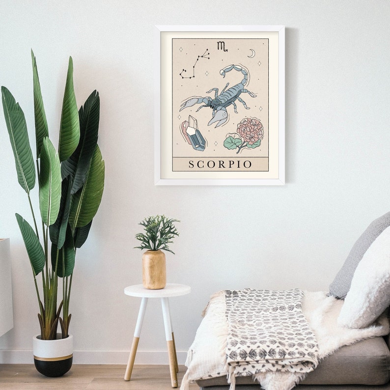 Pu&ograve; includere: Una stampa incorniciata bianca con uno sfondo beige che presenta un'illustrazione di scorpione blu, una costellazione, un fiore e cristalli. Il testo "SCORPIO" &egrave; stampato sotto l'illustrazione.