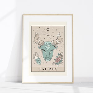 May include: A beige and brown illustrated print of the Taurus zodiac sign. The illustration features a blue bull's head with a constellation of stars above it. The print also includes a crystal and flowers.