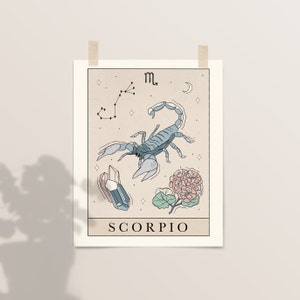 Pu&ograve; includere: Un'illustrazione beige e blu del segno zodiacale dello Scorpione. L'illustrazione presenta uno scorpione, una costellazione, un cristallo e un fiore. Il testo "SCORPIO" &egrave; stampato sotto l'illustrazione.