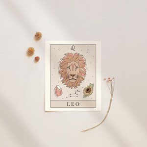 May include: A beige card with a line drawing of a lion's head with a pink mane. The card also features a constellation, a crystal, a sunflower, and the text "Leo" and the astrological symbol for Leo.