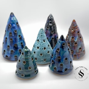 May include: Six ceramic cone-shaped salt cellars in various shades of blue and green with holes throughout. The salt cellars are arranged on a white surface. The text "TURN TURN TURN" and "SALLY SCHRAAMM POTTERY" is visible in the lower right corner of the image.