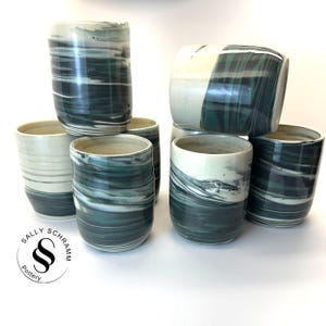 May include: Set of six green and white ceramic mugs with a marbled glaze. The mugs are stacked in a pyramid shape. The mugs are handmade and have a unique, organic look.