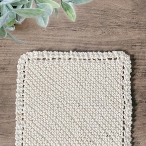 May include: A white knitted dishcloth with a crocheted border. The dishcloth is made of cotton yarn and is perfect for cleaning dishes or drying hands.