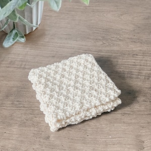 May include: A white crocheted dishcloth or kitchen towel folded on a wooden surface.