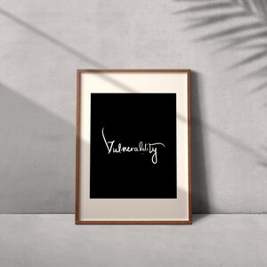 May include: A framed print with a black background and white text that reads "Vulnerability". The frame is brown wood.