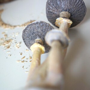 May include: Two ceramic mushroom sculptures with brown caps and beige stems. The mushrooms are stacked on top of each other.