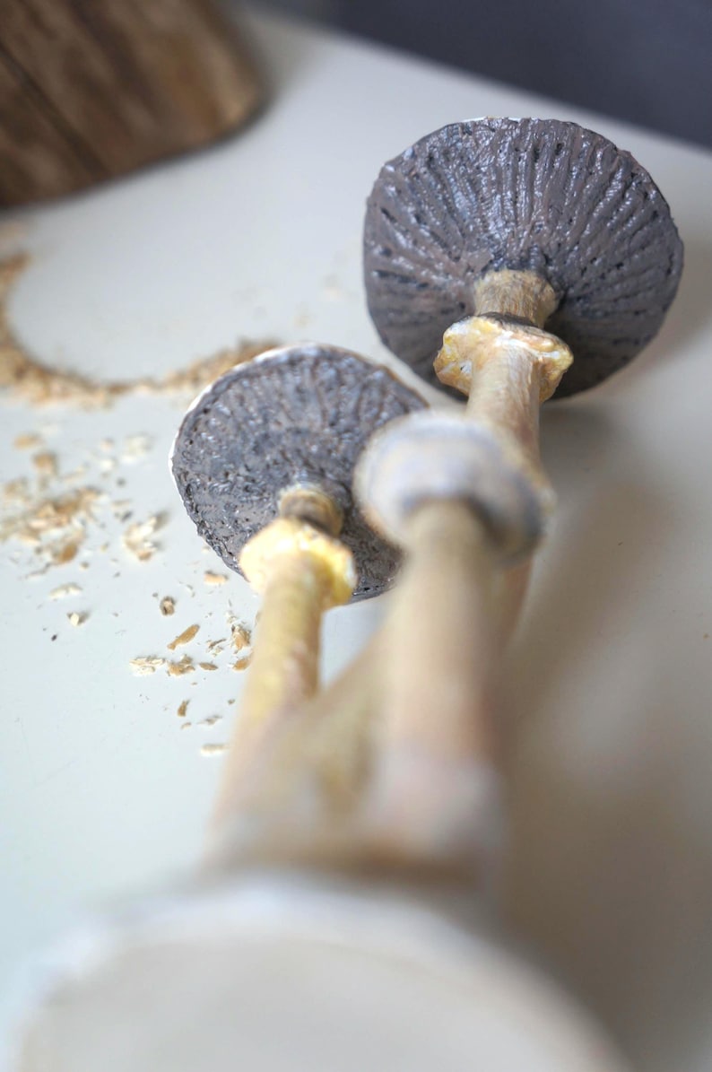 May include: Two ceramic mushroom sculptures with brown caps and beige stems. The mushrooms are stacked on top of each other.