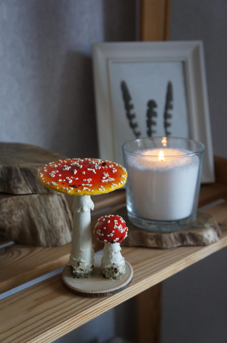 May include: A decorative shelf arrangement featuring two ceramic mushroom figurines with red and white spotted caps. A lit candle in a glass jar and a framed print are also on the shelf. The shelf is made of wood.