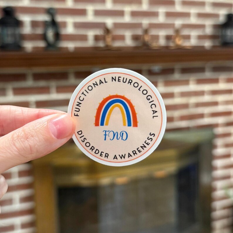 A circular sticker with a light orange background featuring a blue and orange awareness rainbow in the middle with "FND" underneath. The words "Functional Neurological Disorder Awareness" wrap around the design.