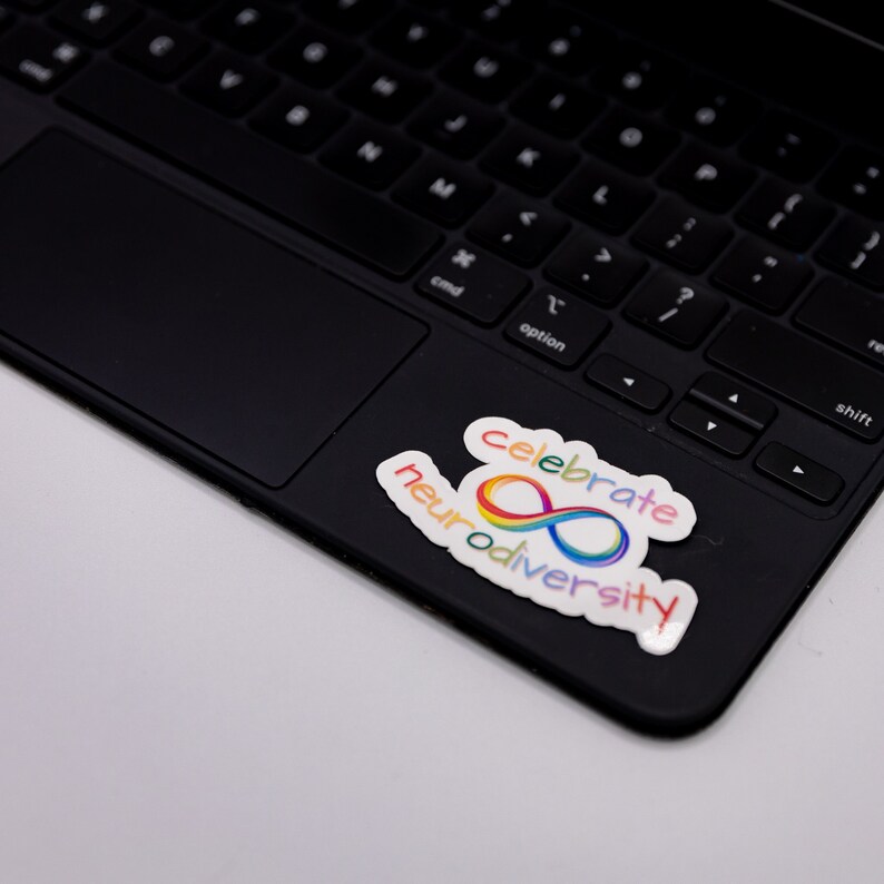 A rainbow sticker that says "celebrate neurodiversity" featuring a rainbow infinity sign. The sticker is on a laptop.