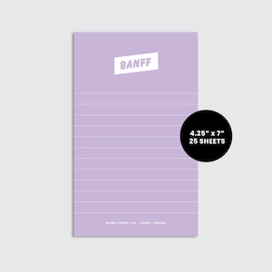 May include: A lilac notepad with horizontal lines and the word "BANFF" in a white, angled rectangle. The notepad measures approximately 10.8cm x 17.8cm and contains 25 sheets. The bottom of the notepad reads "WILDLY SUPPLY CO. BANFF, CANADA."