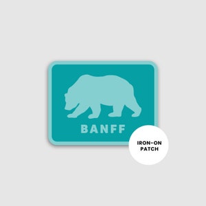 May include: Teal blue iron-on patch with a white silhouette of a bear and the word "BANFF" in white text.